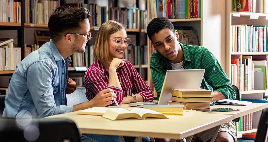 Drei Studierende sitzen in einer Bibliothek und lernen zusammen